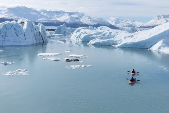 Two kayaks in a serene icy lake surrounded by glaciers and snow-capped mountains.