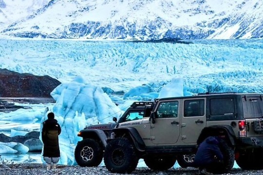 Person and Jeep parked by a snowy landscape with blue ice formations.