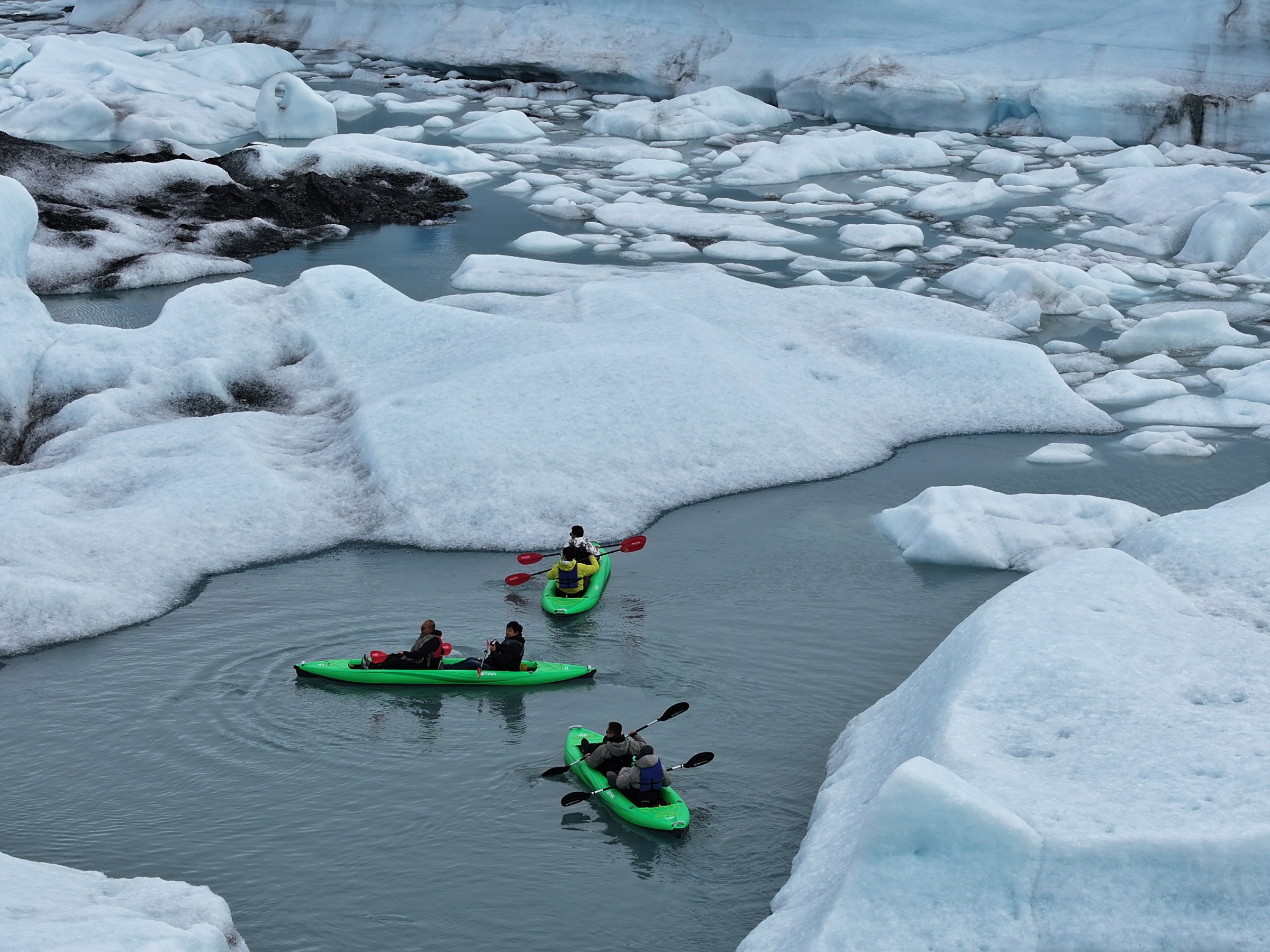 People kayaking among icebergs in a glacial lagoon.